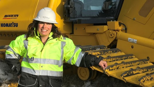 Kim Erion wearing hard hat and reflective jacket leaning against a bulldozer