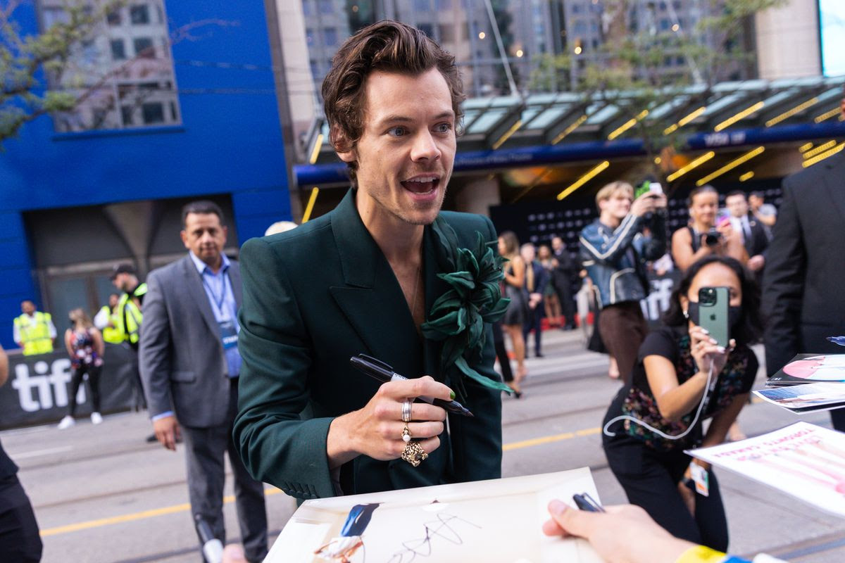 Harry Styles signing autographs on a city street.
