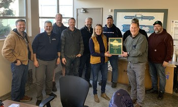 Several people posing for a photo with two in the front holding a plaque