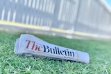 A rolled up copy of the Morning Bulletin newspaper sits on a green grass lawn.