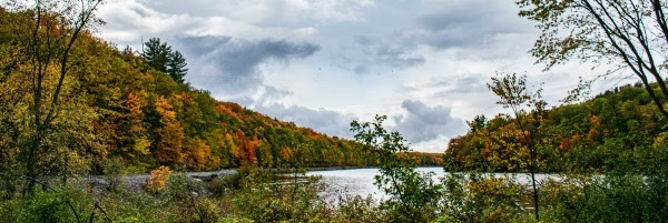 A calm, autumnal lake framed by a forest of orange, red, yellow, and green trees.