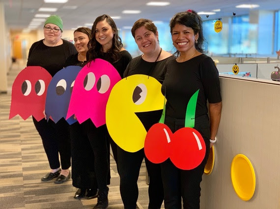 Five WDE staff wear halloween PacMan Halloween costumes. Everyone is dressed in black with posterboard hanging around their neck that shows PacMan, cherries, and three of the ghosts that chase PacMan throughout the game.