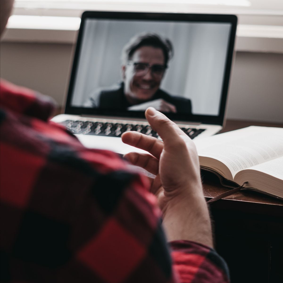 A person in a red shirt sitting in front of a computer talking in a video call to another person. 