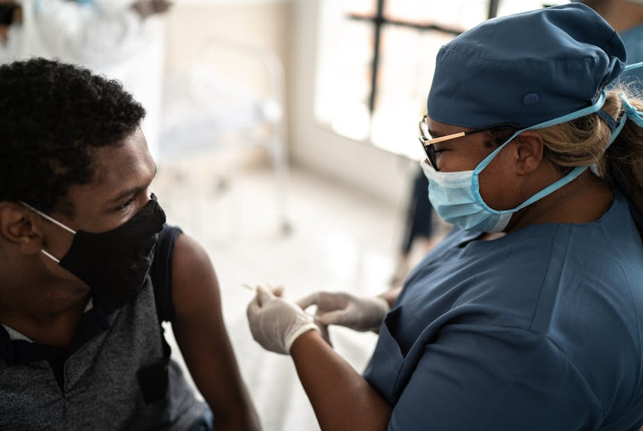 A teen receives a COVID-19 vaccine from a health care worker.