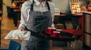 A young woman busses tables in a dimly lit restaurant.