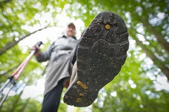 Looking up at the bottom of a man's hiking shoe, with dirt and crushed leaves on the treaded sole