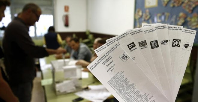 Una persona muestra las papeletas de los diferentes partidos que concurren a las elecciones al Parlamento Catalan que se celebran hoy en Cataluña, mientras una persona deposita su voto en la urna en una jornada en la que un total de 5.314.736 personas est