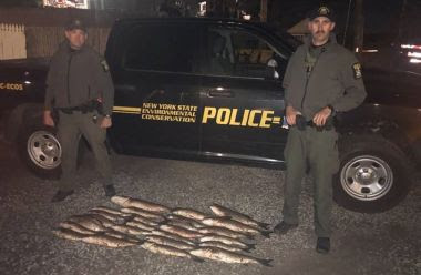 two ECOs stand with large dead fish that were confiscated between them