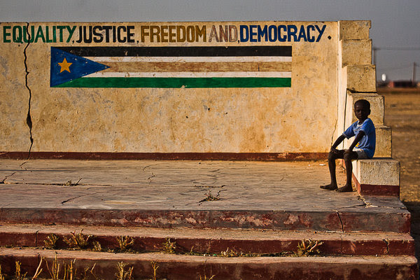 In South Sudan, a child sits by a wall painted with the flag of the world’s newest nation.