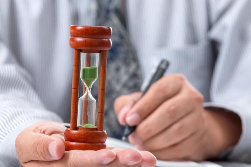 Close up hour glass laying on right hand of businessman taking note