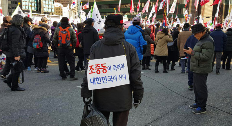 18일 태극기 집회 참가자의 등 뒤에 '조중동이 죽어야 대한민국이 산다'는 피켓이 붙어 있다.