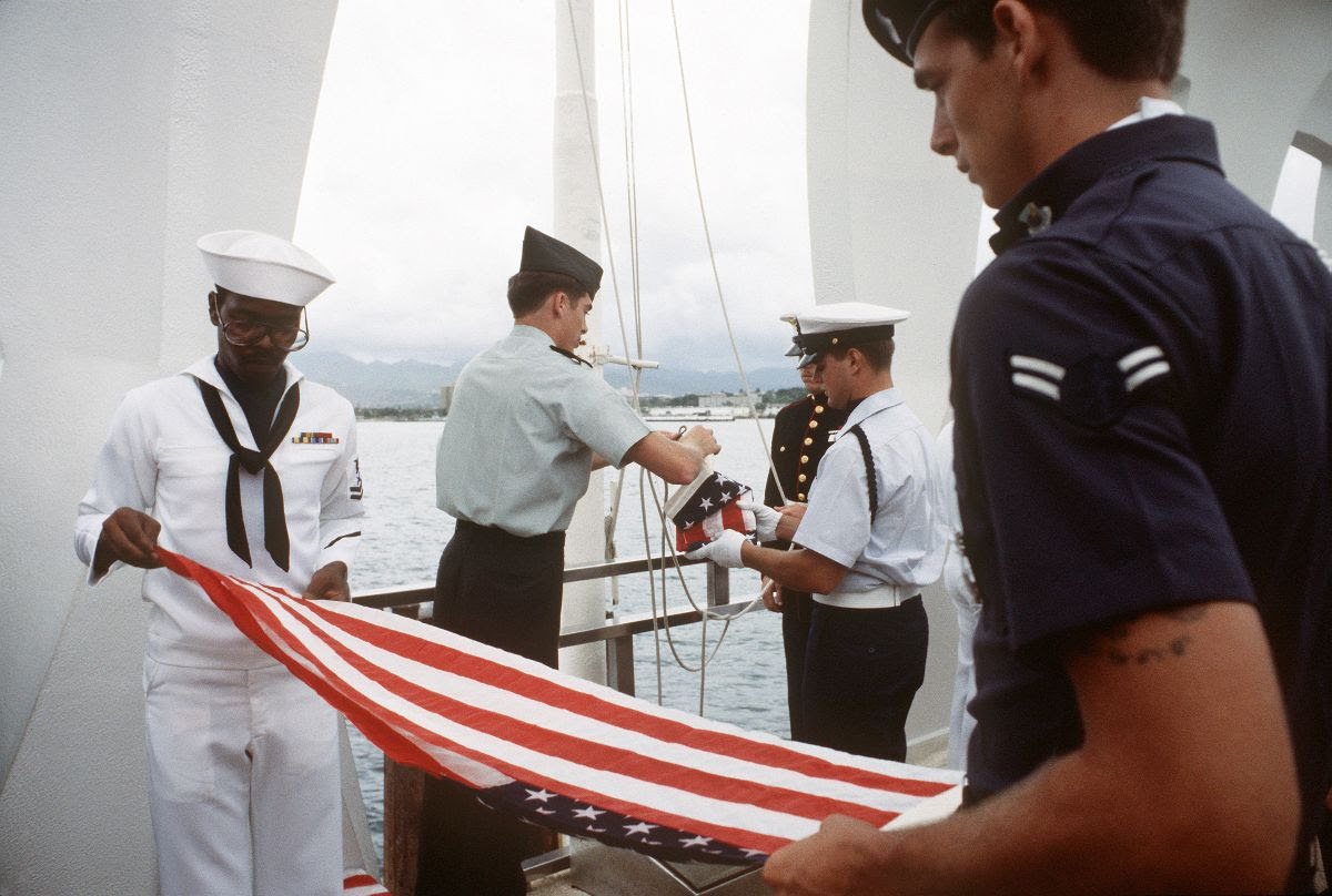 US serviceman on board the USS Arizona memorial folding an American flag as they retire the colors