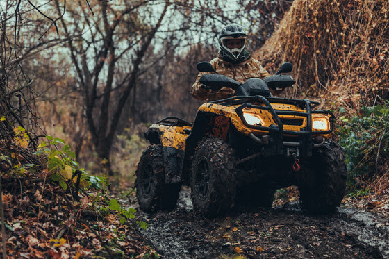 Unrecognizable person driving fix quad on a muddy path through the forest