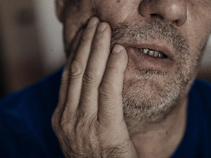 close up of man whose teeth hurt, holding hand over jaw