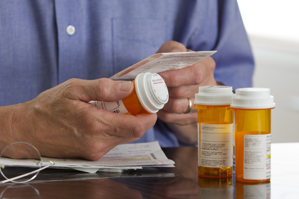 man in a blue shirt, reading prescription bottle and accompanying information print out