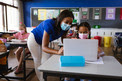 teacher in mask helping student in mask on laptop