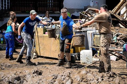 People passing buckets filled with muddy water surrounded by debris.