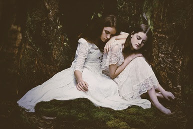 Two girls in white dresses sit together.