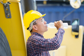 Worker in a hard hat drinks water to avoid heat stress