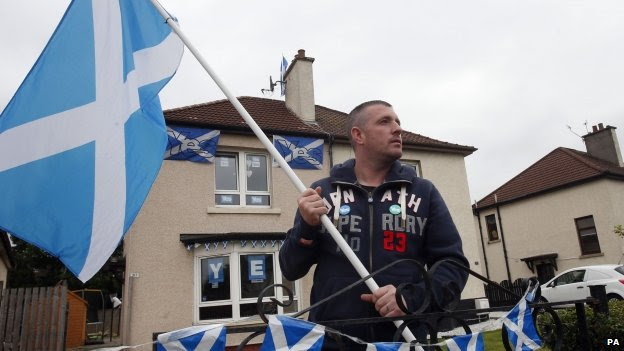 A Scotsman waves a Scottish flag outside his home