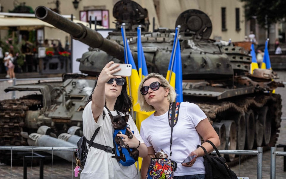 Two women pose for a selfie in front of a destroyed Russian tank CREDIT: Wojtek RADWANSKI / AFP