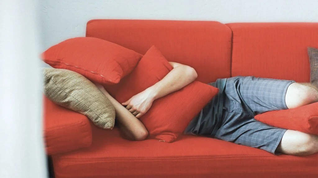 Someone asleep on a sofa under red cushions
