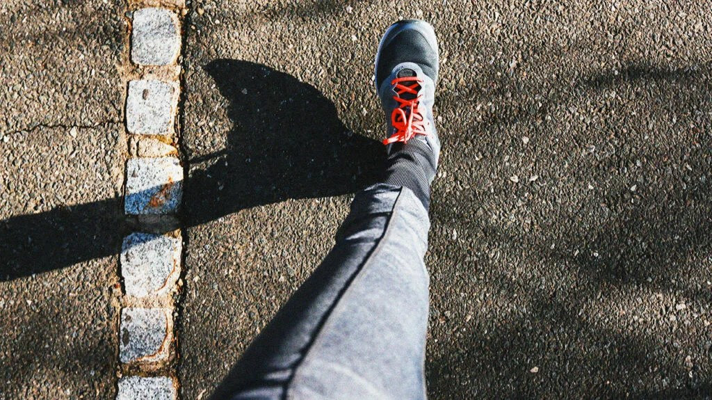 A person's leg outstretched as they walk along a pavement, seen from above.