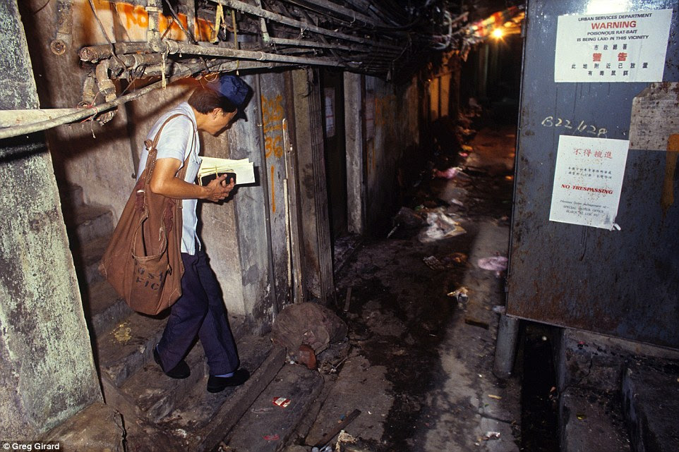 A postman ducks under pipes and cables as he delivers mail to residents who lived along a rat-infested alley covered in rubbish