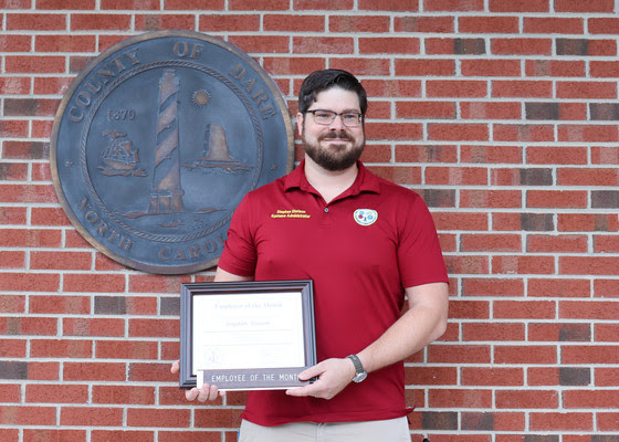 Image of Stephen Stetson standing in front of a brick wall holding his Employee of the Month certificate.