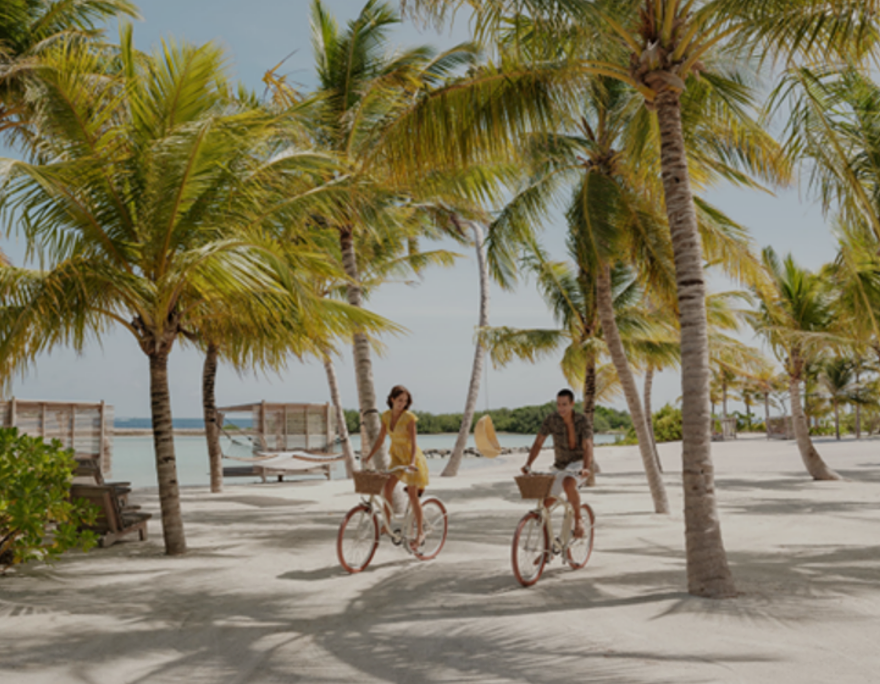 A couple riding bicycles on a beachDescription automatically generated