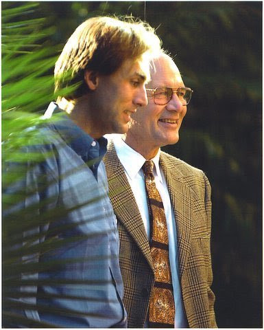 Erik and Ed smiling. Erik is wearing a blue button down; Ed is wearing a brown blazer, white shirt, and patterned brown tie. 