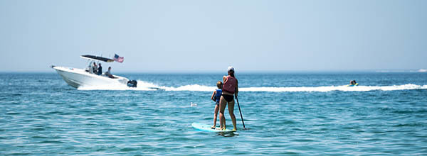 speedboat in the background with mother and daughter paddle boarding