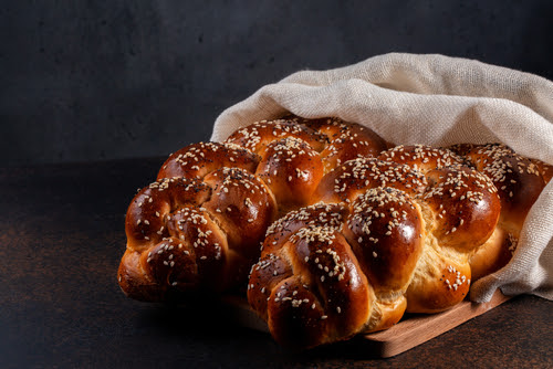 Homemade Challah bread with white cover_ Jewish cuisine. Main ingredients are eggs_ white flour_ water_ sugar_ salt and yeast. Decorated with sesame and poppy seeds. Dark background.