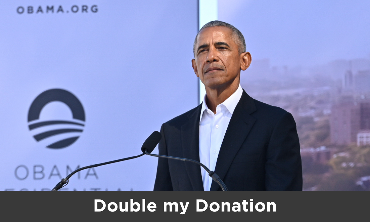 President Obama looks thoughtfully into the distance behind a podium with two microphones on it. He wears a dark suit jacket with a white collared shirt. Behind him, a sign partially shows “Obama Foundation” with the rising sun logo, as well as a portion of a rendering of the Obama Presidential Center campus.