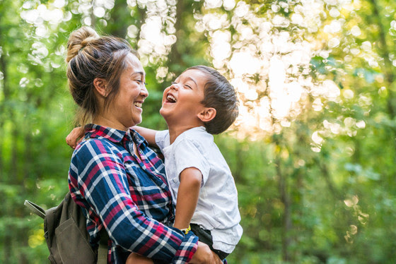 A laughing young mixed-race mother holding her son enjoy time in nature together.   