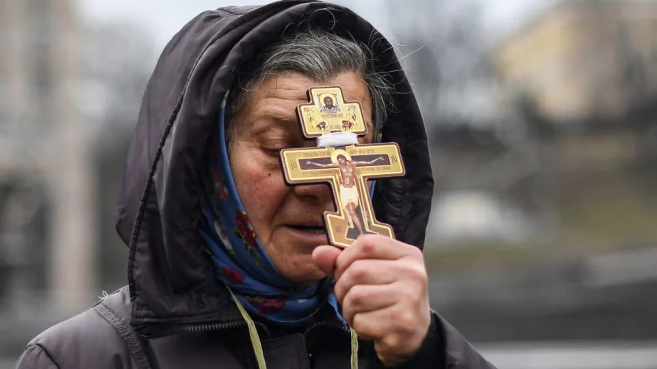 A religious woman holds a cross as she prays on Independence Square in Kyiv in the morning of Feb. 24, 2022. <span class=copyright>Daniel Leal/AFP via Getty Images</span>
