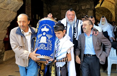 A Jewish father and son at
                  the Western (Wailing) Wall in Jerusalem share the
                  burden of carrying the heavy Torah scroll. (Photo by
                  Reinhardt Konig)