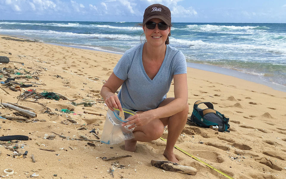 A woman crouches on the beach, putting small pieces of trash into a plastic bag.