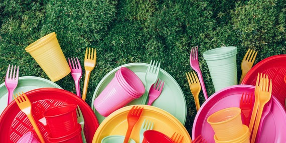 An assortment of brightly coloured single use plastic crockery on the grass