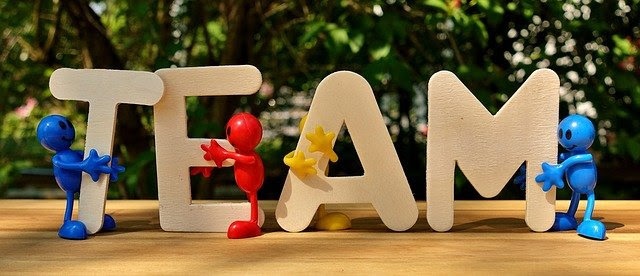 Bendy plastic figurines hugging wooden letters that spell the word "team"
