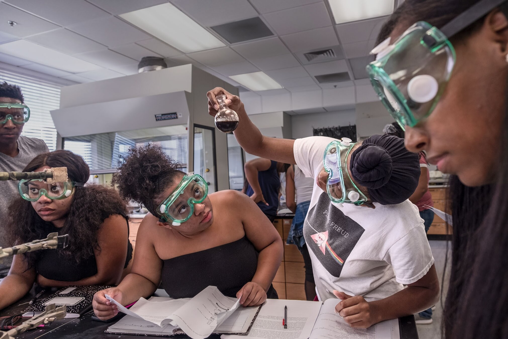 5 young black student engaging with notebooks and liquids during a chemistry class