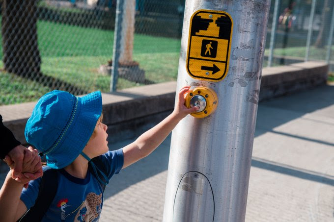 A child in a blue hat is pressing a pedestrian signal button.