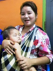 A baby naps in his mother's arms outside the flu vaccination clinic at Vientiane's busy maternal hospital. Laos, 2012.