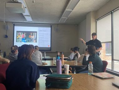 ECO points to projector screen while speaking with college students
