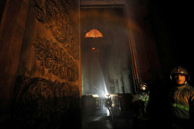Slide 3 of 31: Paris Fire brigade members are seen at an entrance that looks into the Notre Dame Cathedral as a fire continues to burn in Paris, France, April 15, 2019. REUTERS/Philippe Wojazer
