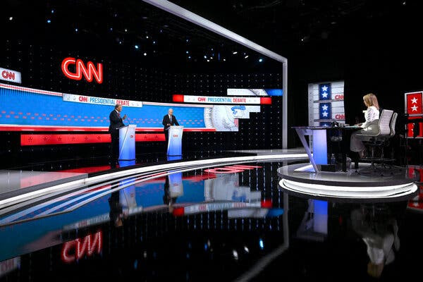 President Biden and Donald Trump at their lecterns on the debate stage, in the background at left, and the debate moderators in their chairs, right. The CNN logo hangs high above the candidates on the wall in the background.