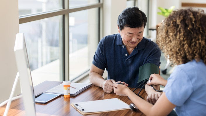 Nurse taking older male patient's blood pressure at a medical office.