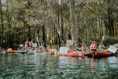kayaks in beautiful river with people holding signs to protect santa fe florida