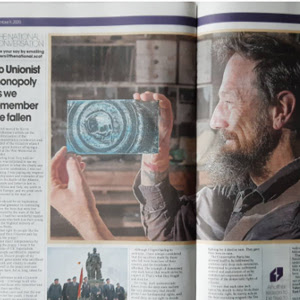 A photograph of a newspaper spread featuring a large image of a maker holding a glass work.