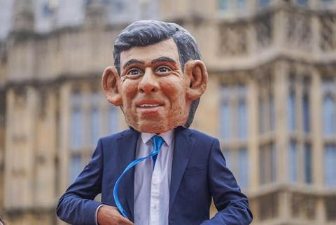 A person wearing giant model head of Rishi Sunak outside parliament.